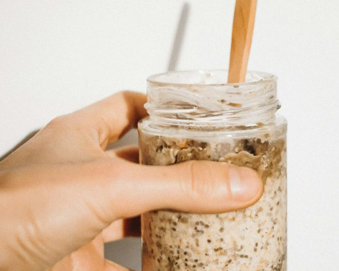persona che tiene in mano un bicchiere con latte e avena in fiocchi